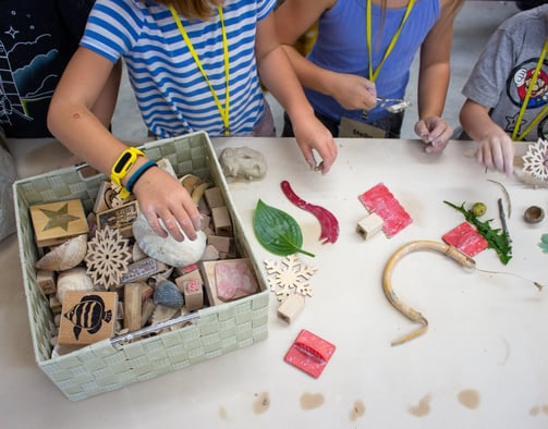 Children's hands reaching into a bin of stamps and supplies.