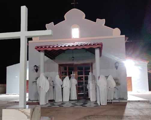 Penitentes de branco em frente à capela, em ritual noturno de fé e arrependimento em São Tomé