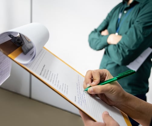A person writing on paper on a clipboard