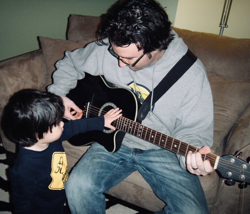 A father sitting while playing guitar with his toddler
