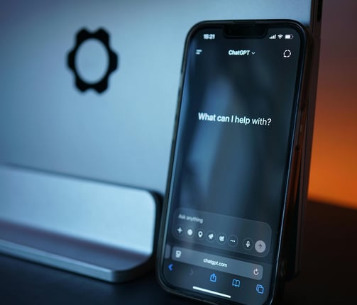 a phone in front of a laptop with ChatGPT on the screen