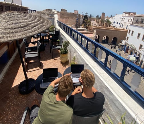 two men sitting at a table with laptops