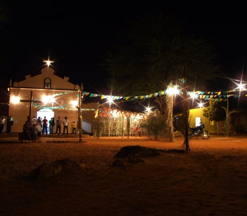  Igreja iluminada com bandeirolas e pessoas reunidas na Festa de São João à noite