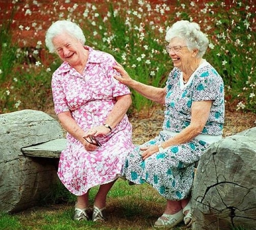 Two senior women laughing together, sitting outside