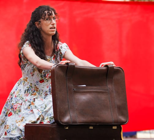 comédienne chanteuse sur scène équipée d'un micro serre tête, en train d'ouvrir une valise