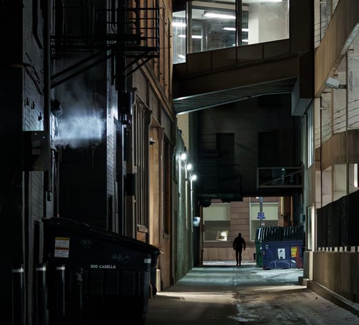 Moody and cinematic image of a silhouetted man walking down a city alley at night.