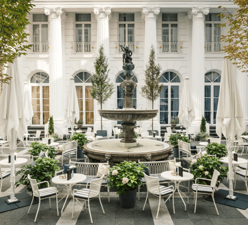 Ein Springbrunnen in einem Innenhof mit weißen Stühlen und Tischen.