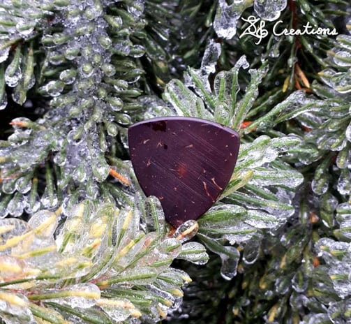 One of our Pythagorean coconut shell guitar picks on top of ice covered pine branches.