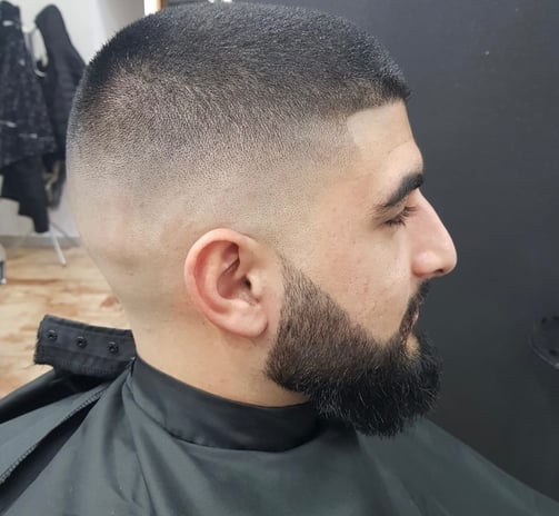 Taglio sfumato alto con barba rifinita su uomo con capelli corti e scuri, eseguito in salone da barb