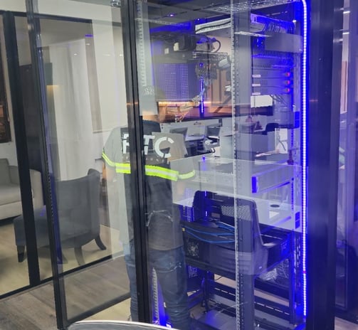 Técnico trabajando dentro de cuarto de servidores con gabinete iluminado.