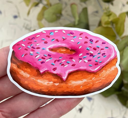 a hand holding a pink donut with sprinkles of sprinkle