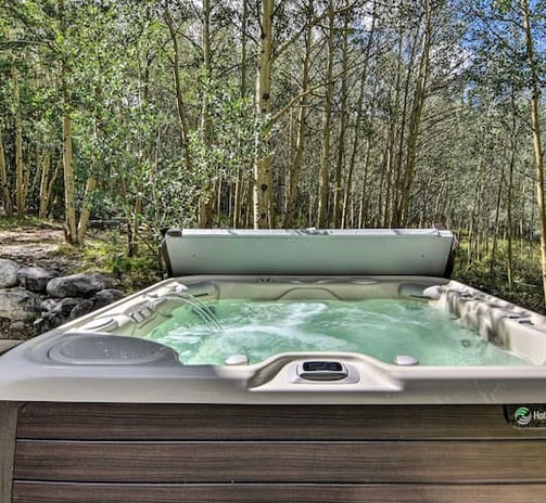 Hot tub with open lid and bubbling water in a forested backyard