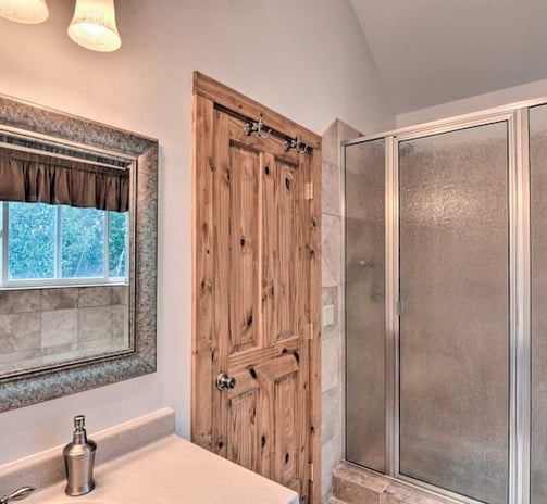 Rustic bathroom view with a wooden door, vanity mirror, and glass shower enclosure.
