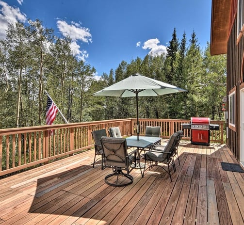 Spacious deck at Moose Creek Lodge with dining table, umbrella, gas grill, and forest views.