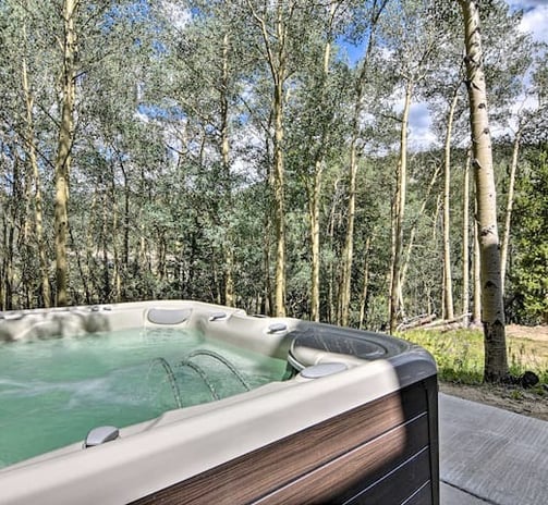 Outdoor hot tub surrounded by tall aspen trees under blue sky