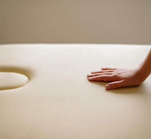 Relaxing atmosphere, one hand is placed on the cream-colored massage table