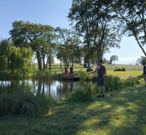 a man standing in a field with a boat in the water