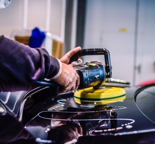 Técnico realizando pulido profesional de la pintura del coche con máquina pulidora.