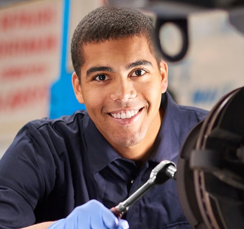 Homem usando jaleco azul e sorrindo para a camera enquanto trabalha