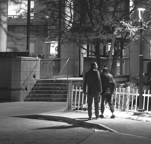 Black and White Photo of a couple walking at night below the glow of a street lamp.
