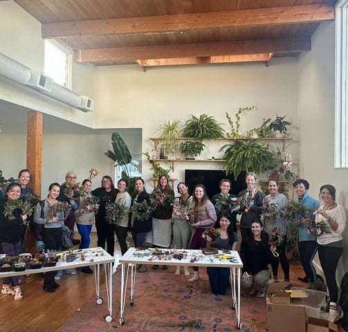 a group of women each holding a wreath standing around a table with plants