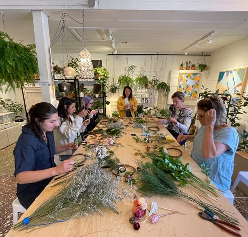 a group of people are gathered around a table during a wreath workshop