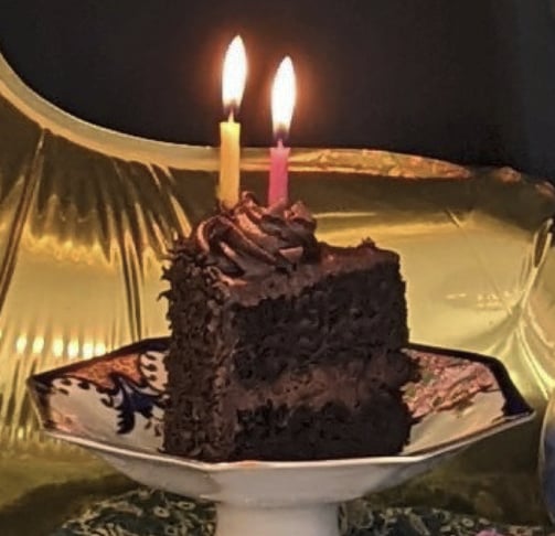 Slice of chocolate cake with burning candles on porcelain trinket tray.