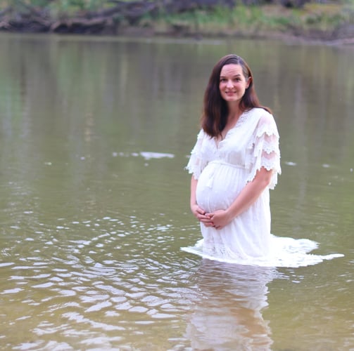 a pregnant woman in a white dress standing in the water