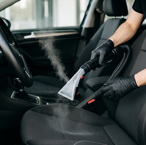 : Detailing technician using steam cleaner to sanitize and deep clean car seats.