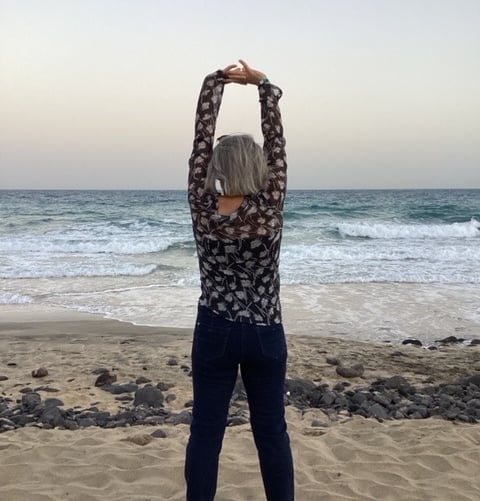 a woman standing on a beach with her arms up in the air