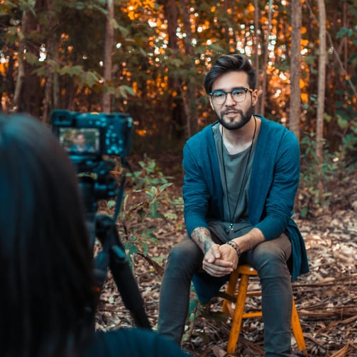 Man being interviewed on camera while sitting in forest 