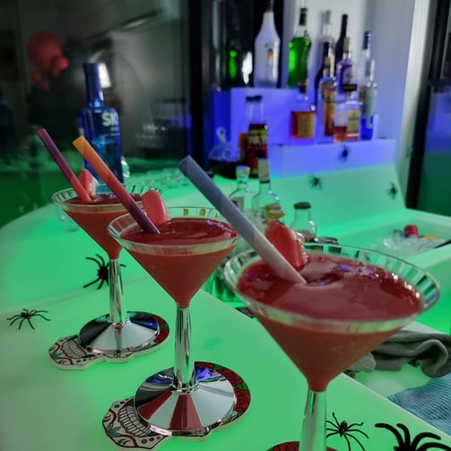 Close-up of three Halloween-themed bloody daiquiris in martini glasses with vampire teeth lolly garnishes, displayed on a glo