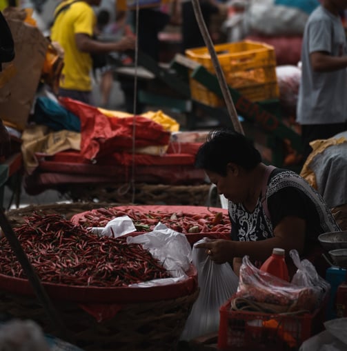 a woman is sitting at a market with many baskets of chili peppers