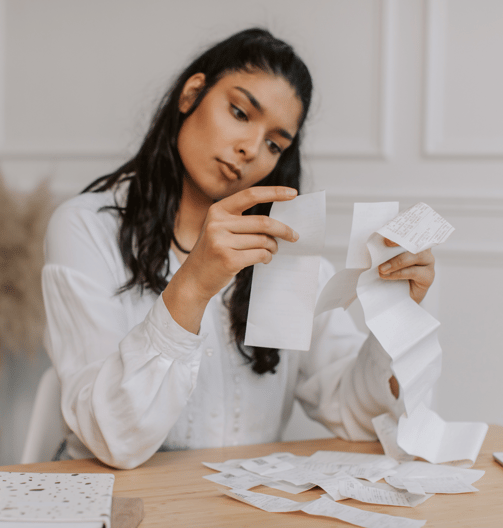 a woman is holding a piece of receipt with a pile of receipts and a notepad