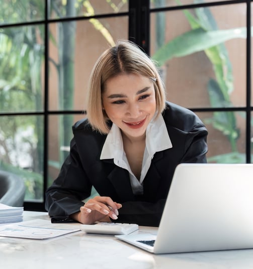 a blonde woman in a suit and tie is smiling and looking at her laptop using a calculator