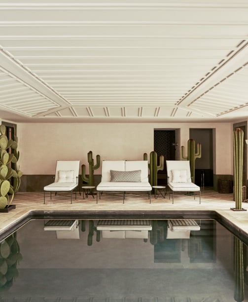 Indoor heated pool at Villa La Gratitud, with lounge beds, potted palms, and garden views beyond.