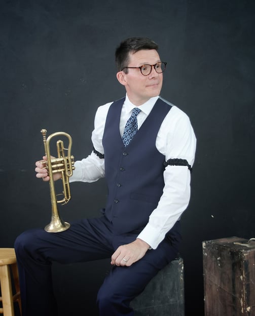 A man in a vest and tie is holding a cornet, looking to the side.