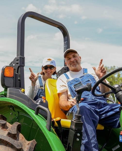 Dr. Norwood on a John Deere tractor giving the "Go Pokes!" sign.