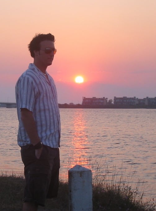 A man standing in front of the ocean with a sunset