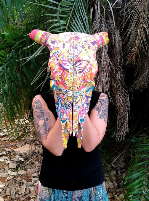 peinture aux couleurs vives sur un crane tenu par l'artiste comme un masque