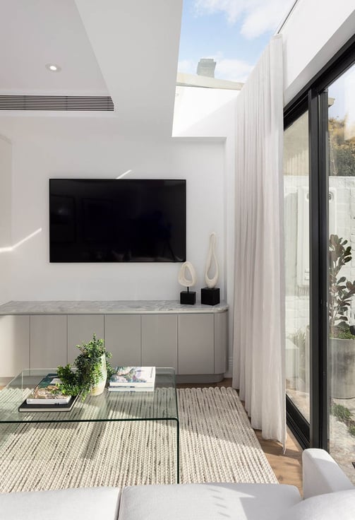 TV area with skylight, soft curtains, wool rug, and glass coffee table in modern living space