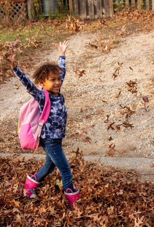 Young girl walking to Access Arts throwing leaves in the air.