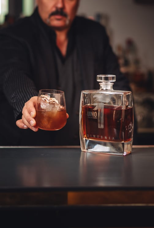 a man in a suit and tie is holding a drink of Luxury Uno Tequila Sinfonia 
