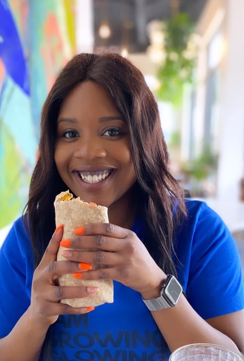 a plus size black woman nutritionist in a blue shirt is holding a sandwich