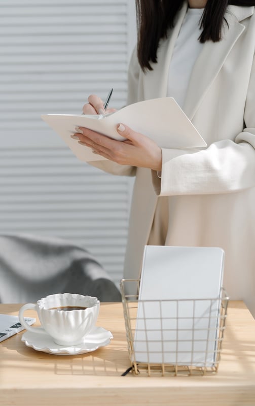 a business woman wearing a white jacket, standing and writing in a notebook