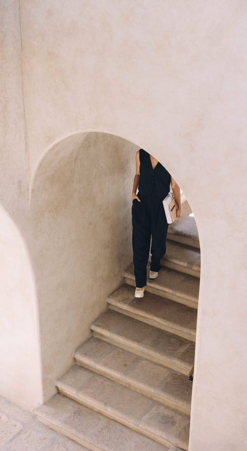 A woman wearing a black top and clacks, carrying a notebook, walking down a marble stairway.
