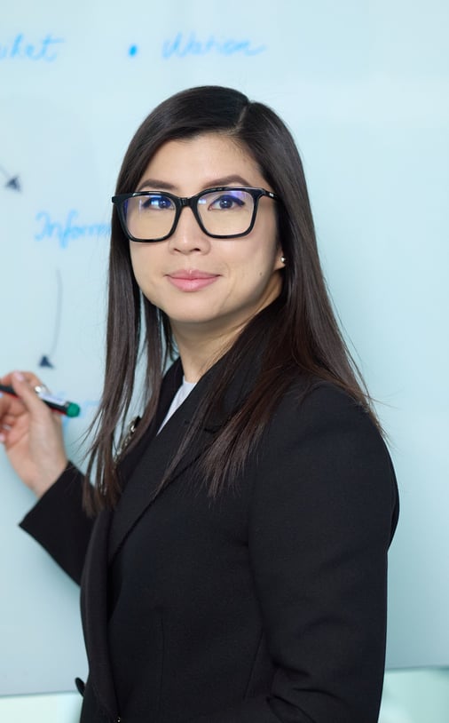 Ka Ming Zwingenberger in a suit and glasses standing in front of a white board with a marker..