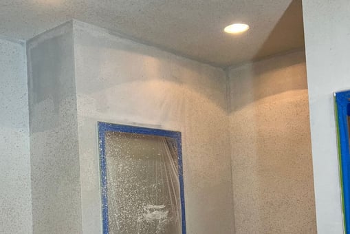 Wall surface with fresh texture spray during interior paint prep, blue painter’s tape and plastic 