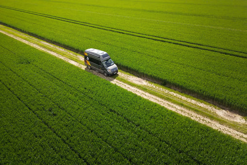 a van driving down a dirt road with a truck