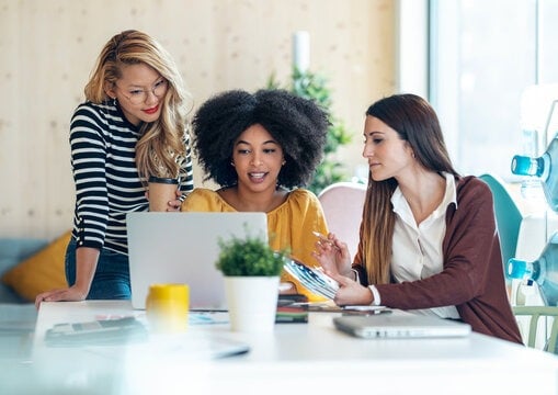 three women sitting at a table viewing a laptop